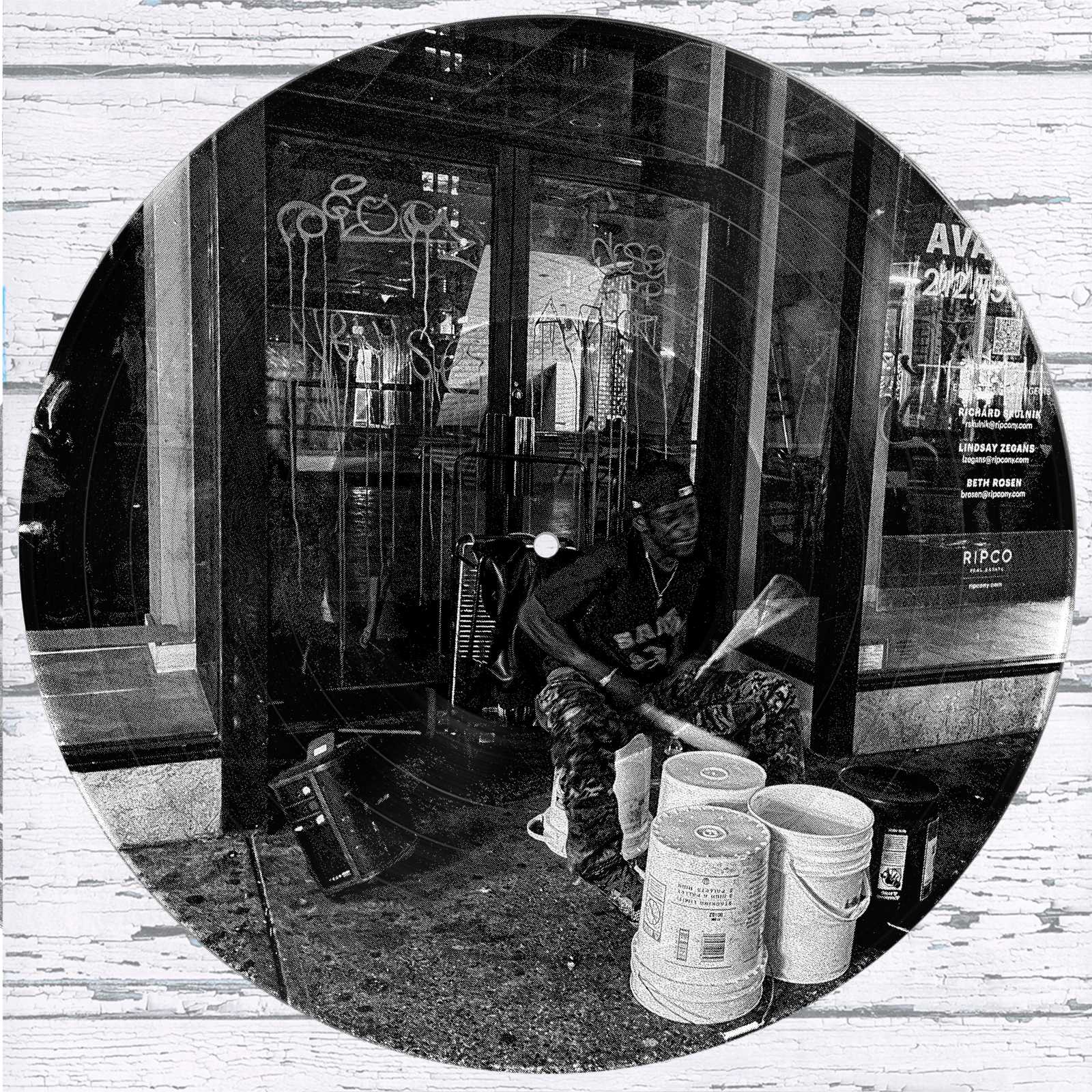 New York City Bucket Drummer vinyl record photo art featuring a black and white photograph of a street drummer performing passionately at night in front of graffiti-covered glass doors.